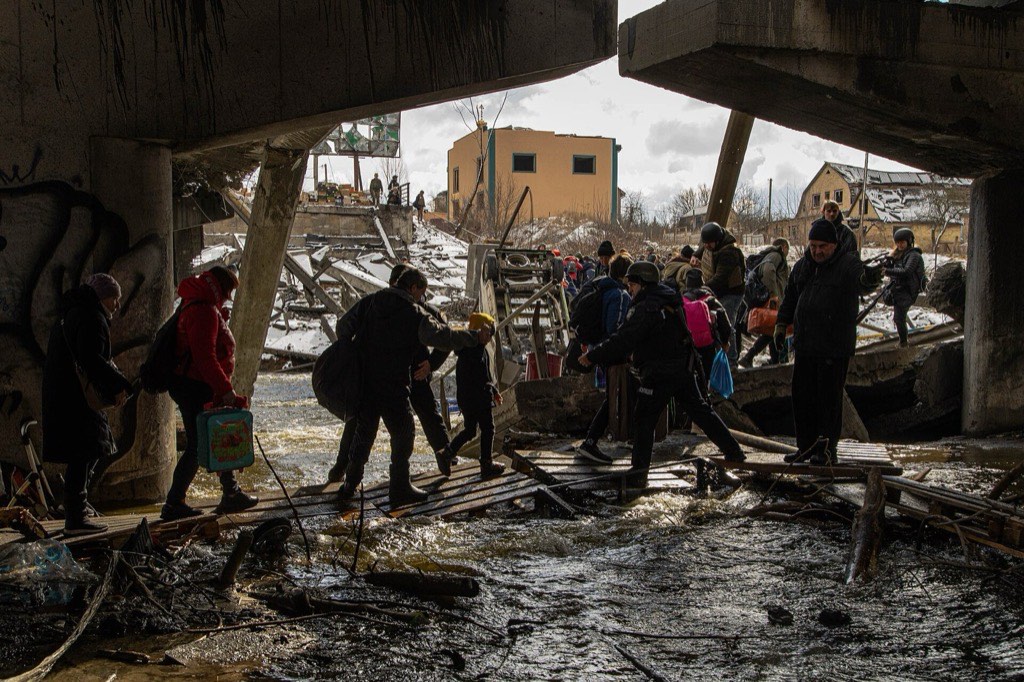 Civilians, including a small child, crossing the destroyed Irpin river bridge on wooden planks while fleeing Russian advance.