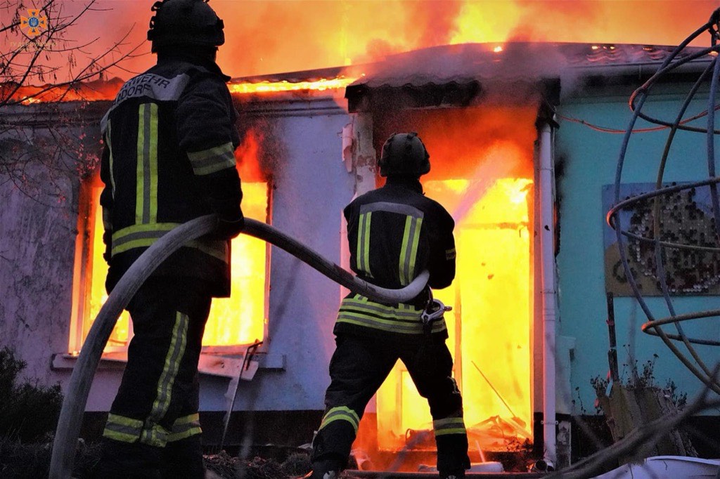 Ukrainian firefighters directing hoses at a kindergarten in Kherson engulfed in flames after Russian shelling.